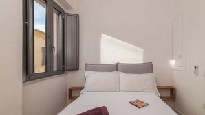 A single bed with white bedding, a pair of rolled towels, and a book on the bed. - David House In The City Center (Olbia)