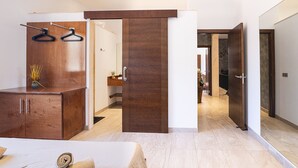 Quarto de hotel moderno com um guarda-roupa de madeira, uma cama com toalha enrolada e um corredor que dá para outro quarto.