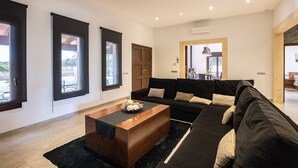 Uma sala de estar moderna com um sofá seccional, uma mesa de centro de madeira e janelas amplas com cortinas escuras.