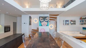 Un intérieur moderne avec un coin repas comprenant une longue table en bois, des chaises transparentes et un lustre.