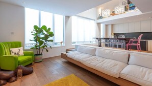 Un salon moderne avec un canapé vert, un canapé blanc et un coin repas doté de chaises transparentes.