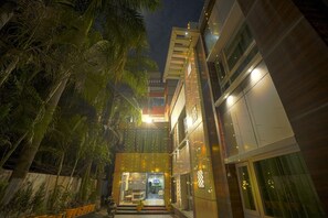 A modern building with a well-lit entrance, surrounded by palm trees. - Q Saina's S K Regency (Narendranagar)