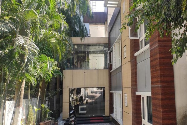 A modern building with a glass entrance, surrounded by lush greenery and potted plants.
