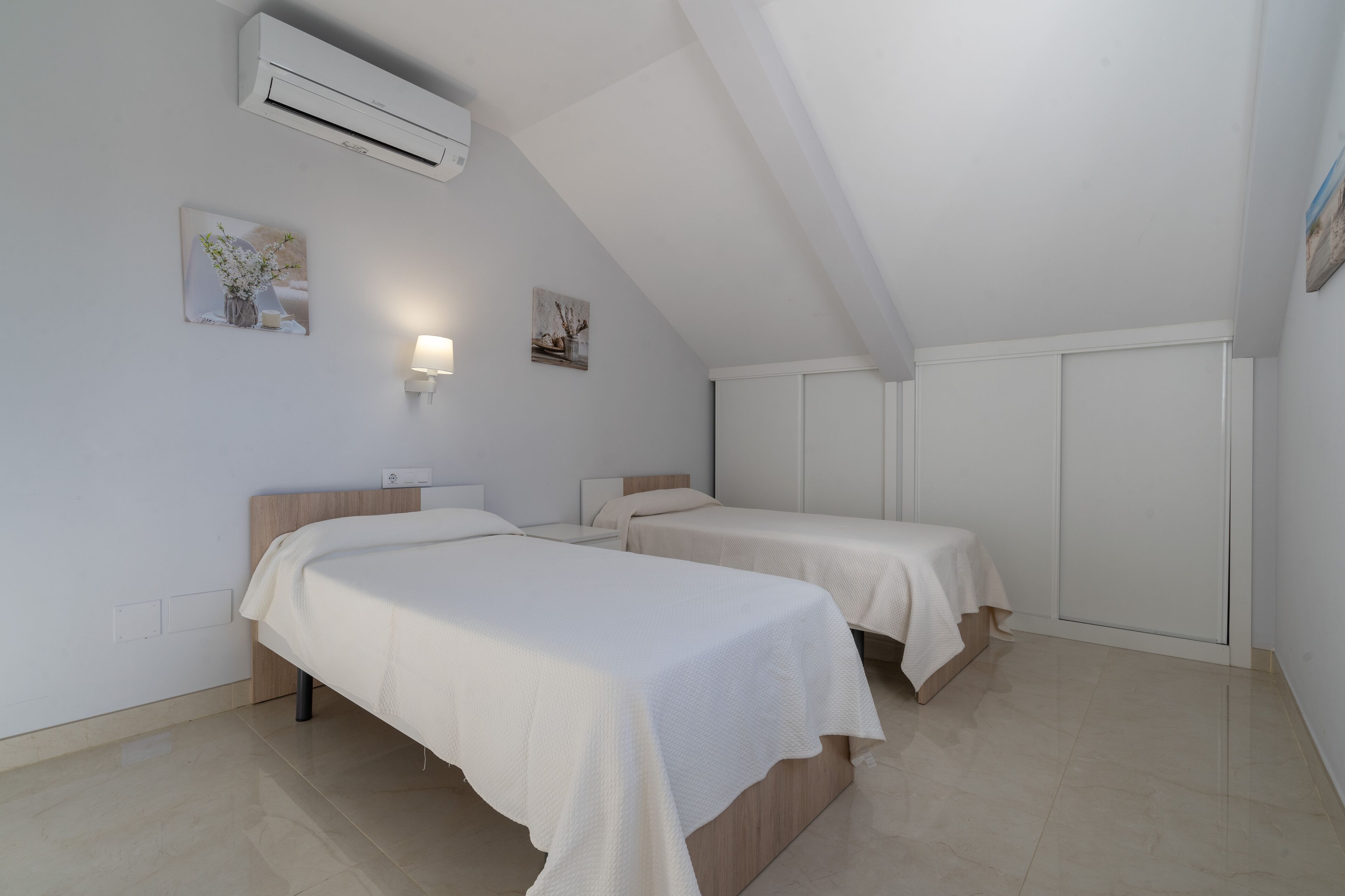 A bedroom with two beds, a ceiling fan, and wall-mounted artwork.