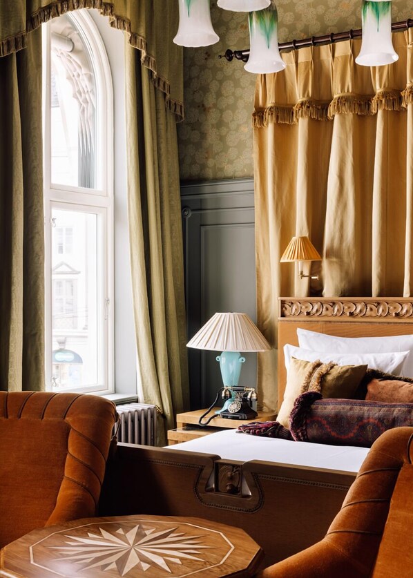 Una habitación de hotel con un ventanal grande, una mesa de madera, un sofá, una lámpara y una cama con almohadas.
