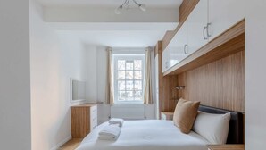 Un dormitorio moderno con una cama grande, cabecera de madera, una mesita de noche, un televisor y una ventana con cortinas.