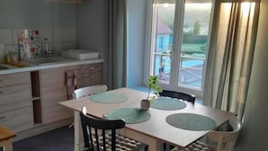 A dining area with a table and chairs, a window with curtains, and a view of the outside. - Gîte du capitaine (Maranville)