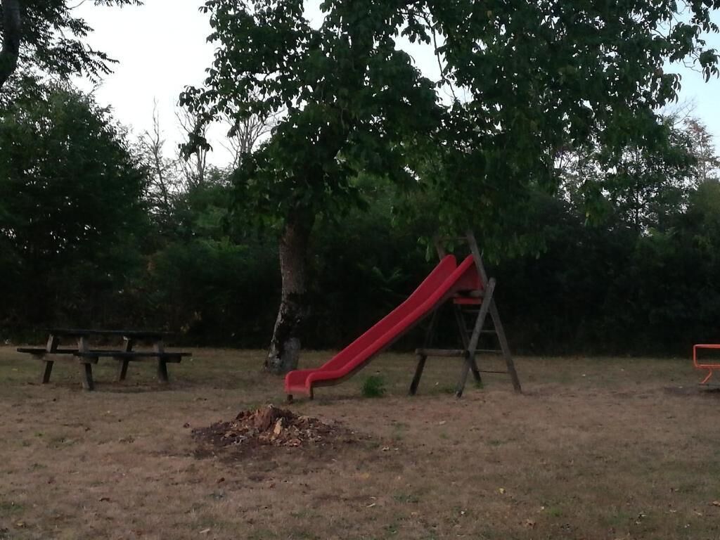 Une aire de jeux avec un toboggan rouge, un banc en bois et un arbre.