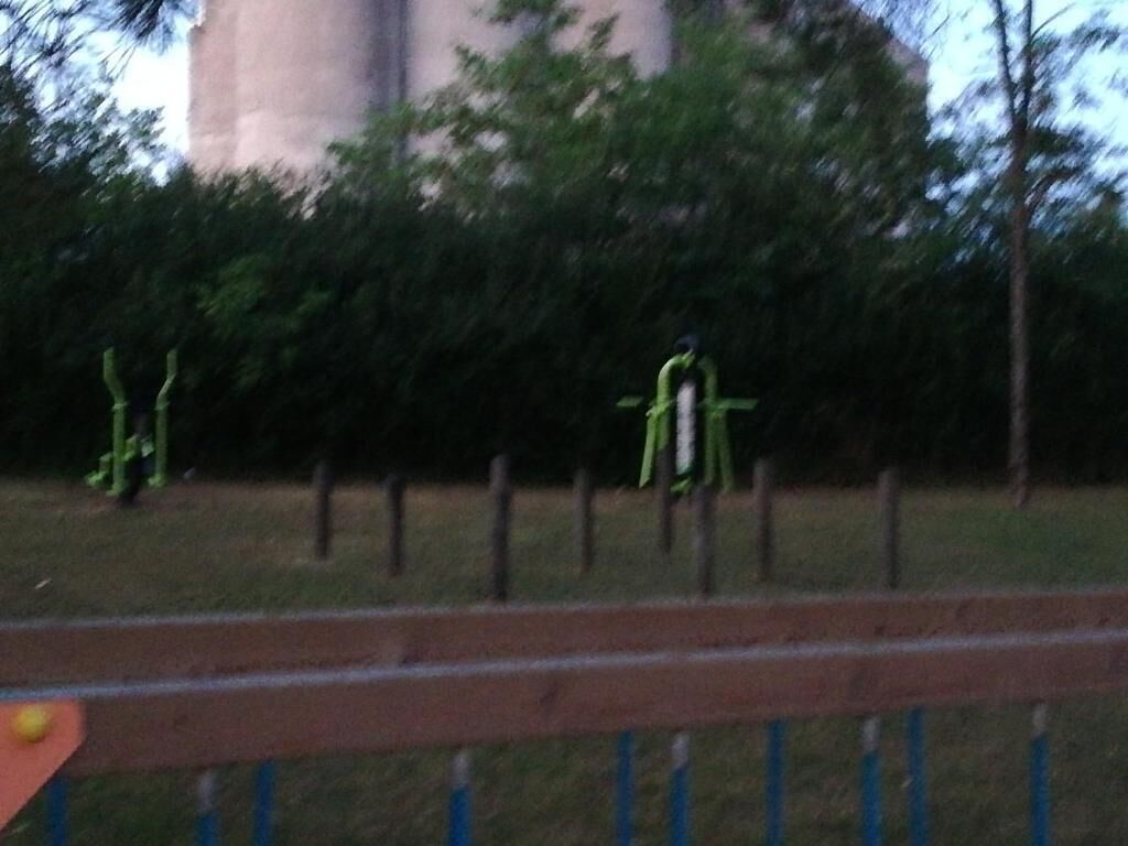 A park with a metal fence, trees, and a large cylindrical structure in the background.