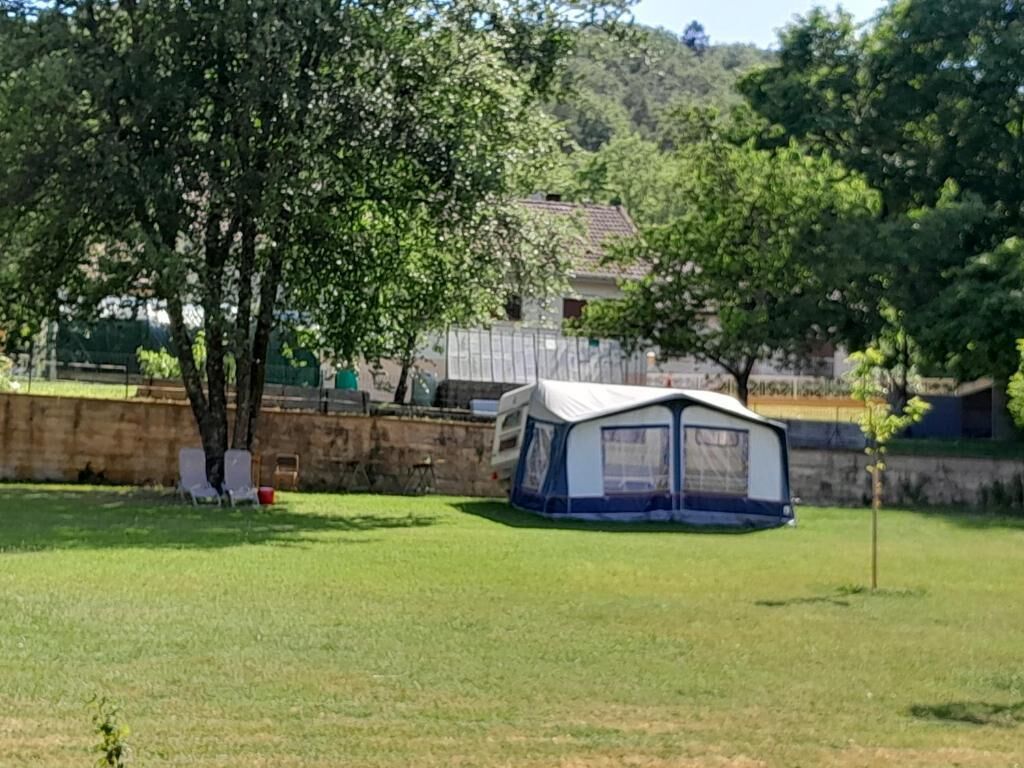 Una tenda in un prato erboso, con alberi e un edificio sullo sfondo.