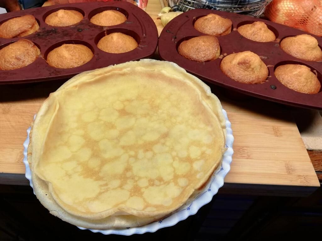 A kitchen counter with a large pancake and muffin tray, and a pie on a plate.