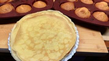 A kitchen counter with a large pancake and muffin tray, and a pie on a plate.