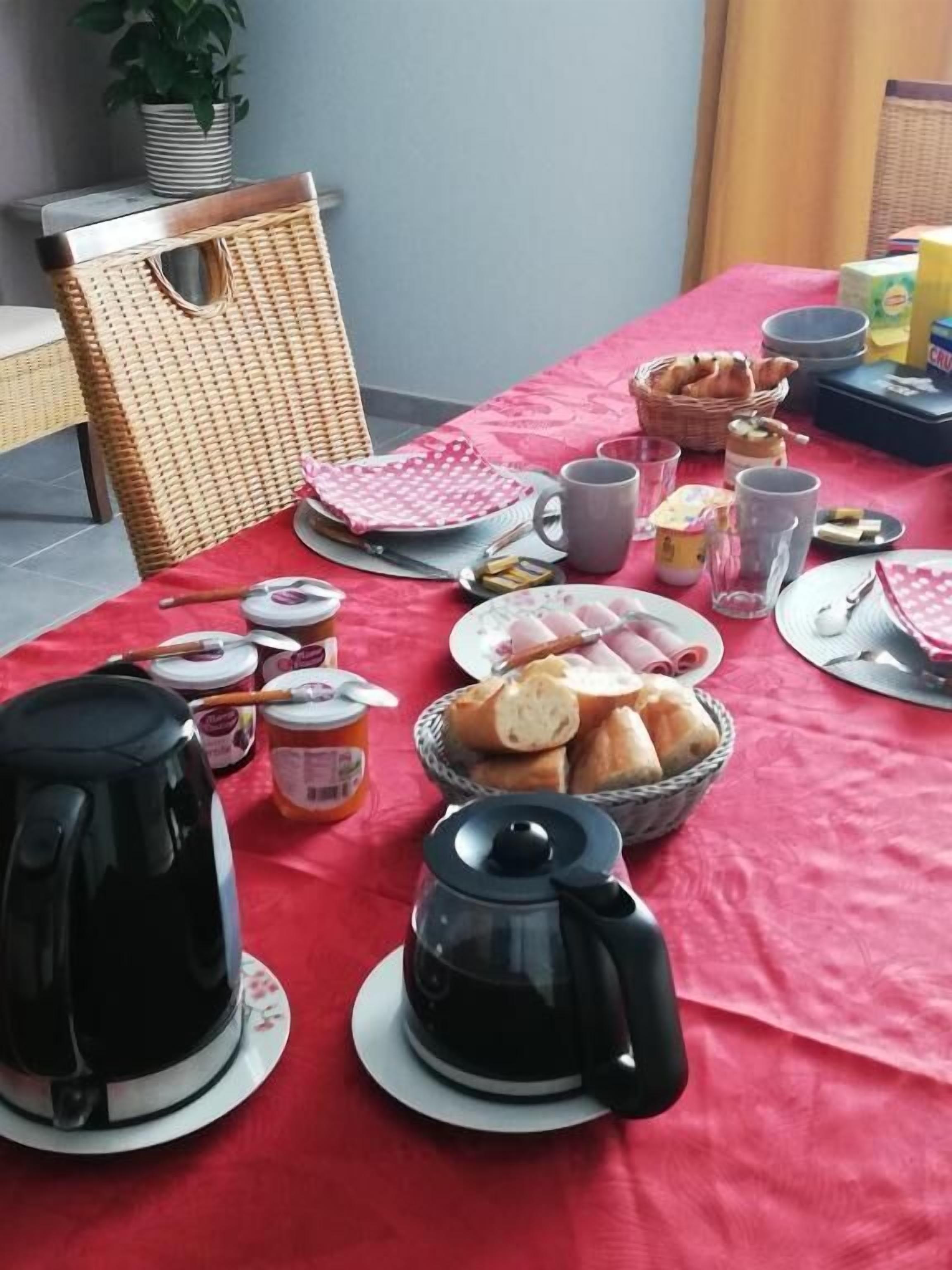 A breakfast setup with a red tablecloth, various breakfast items, and a wicker chair.