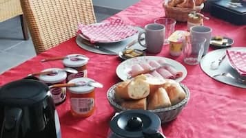 A breakfast setup with a red tablecloth, various breakfast items, and a wicker chair.