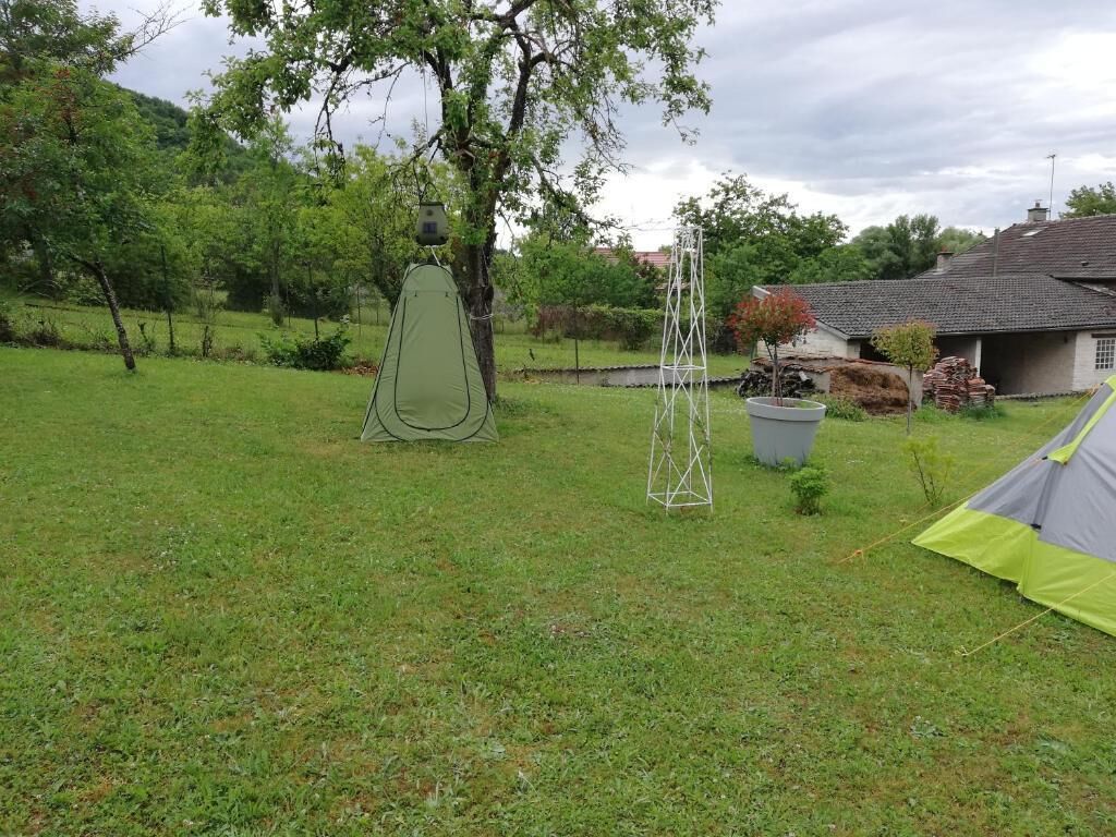 A grassy outdoor area with a tent and a metal structure, likely a tower, in a rural setting with trees and a house in the background.