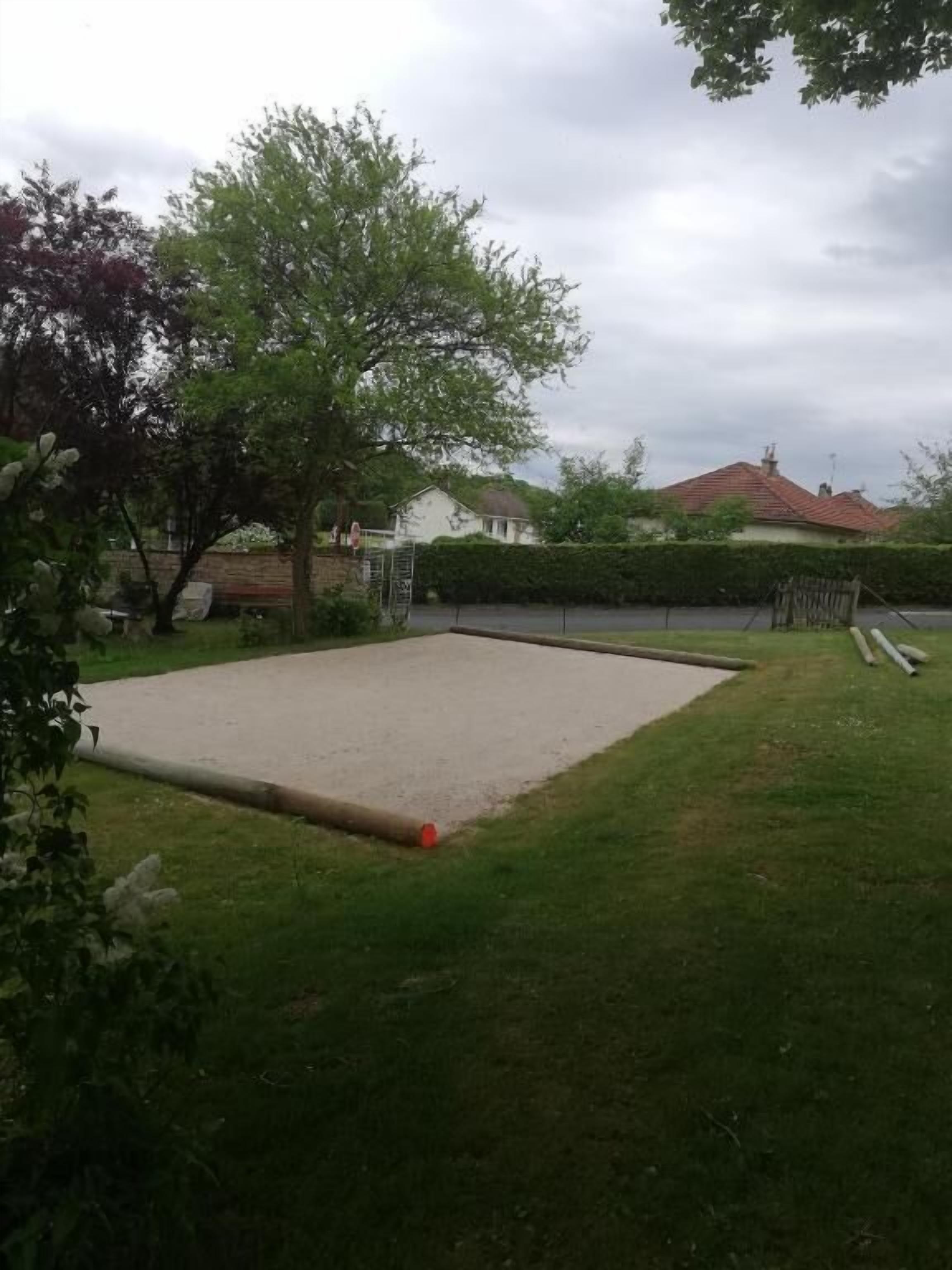 A concrete court with a red ball, surrounded by grass and trees, with houses in the background.
