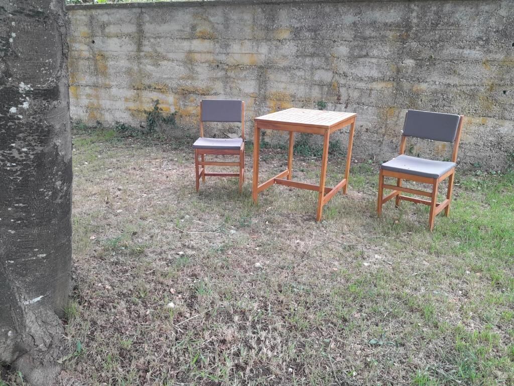Three wooden chairs and a table arranged outdoors against a concrete wall.