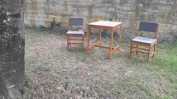 Three wooden chairs and a table arranged outdoors against a concrete wall.