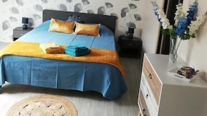 A bedroom with a bed, bedside tables, a desk, a hanging light, and a wall with a leaf pattern. - Gîte du capitaine (Maranville)