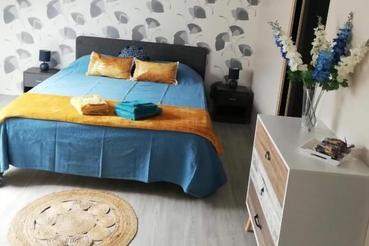 Ein Schlafzimmer mit Bett, Nachttischen, einem Schreibtisch, einer Pendelleuchte und einer Wand mit einem Blattmuster.