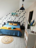 Un dormitorio con cama, mesitas de noche, un escritorio, una lámpara colgante y una pared con estampado de hojas.