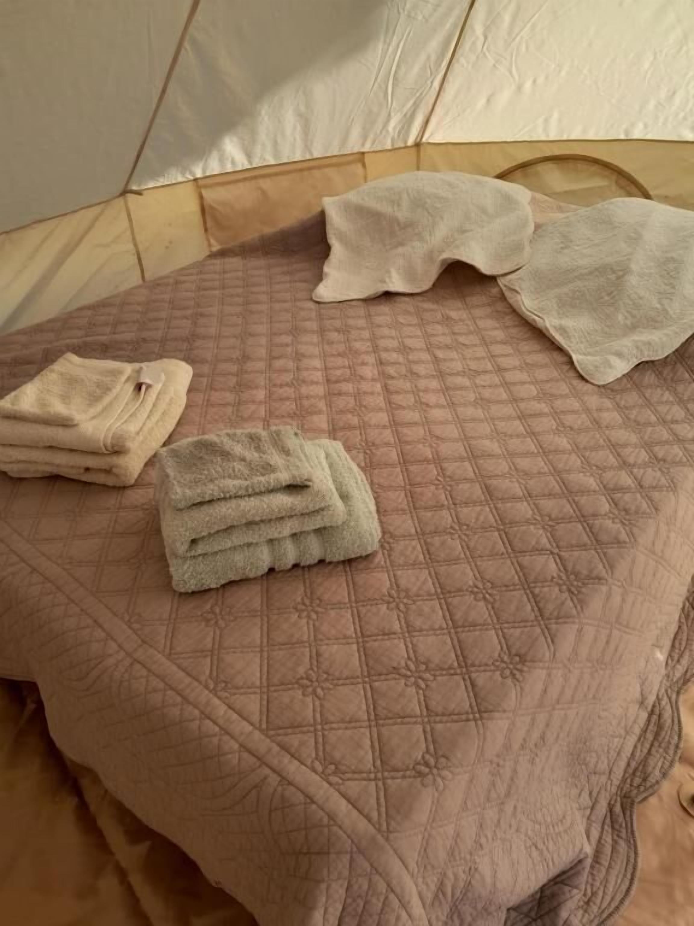A bed with a quilted pink bedspread and two folded towels.