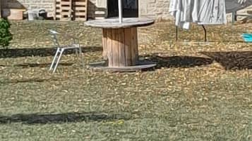 Un espacio patio con una sombrilla roja, una mesa de madera y un muro de piedra al fondo.