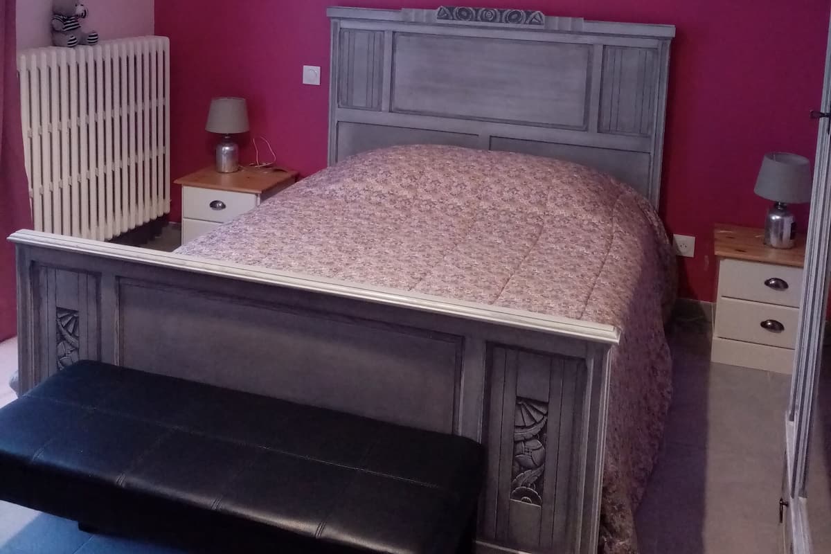 Ein Schlafzimmer mit einem Bett, einer Bank, einem Heizkörper und einer Wandleuchte.