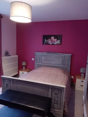 A bedroom with a bed, a bench, a radiator, and a wall-mounted lamp. - Gîte du capitaine (Maranville)