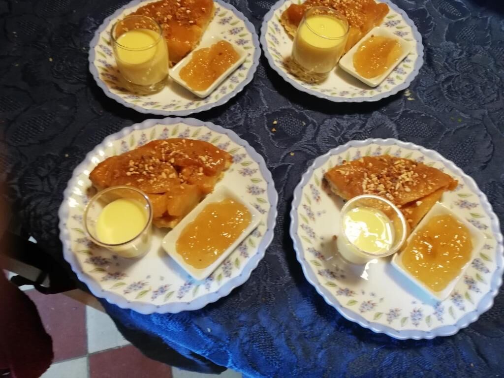 Four plates of food with a glass of a yellow liquid, possibly a sauce or dressing, on a table with a blue patterned tablecloth.