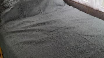 Een bed met een grijs geweven sprei en witte gordijnen.