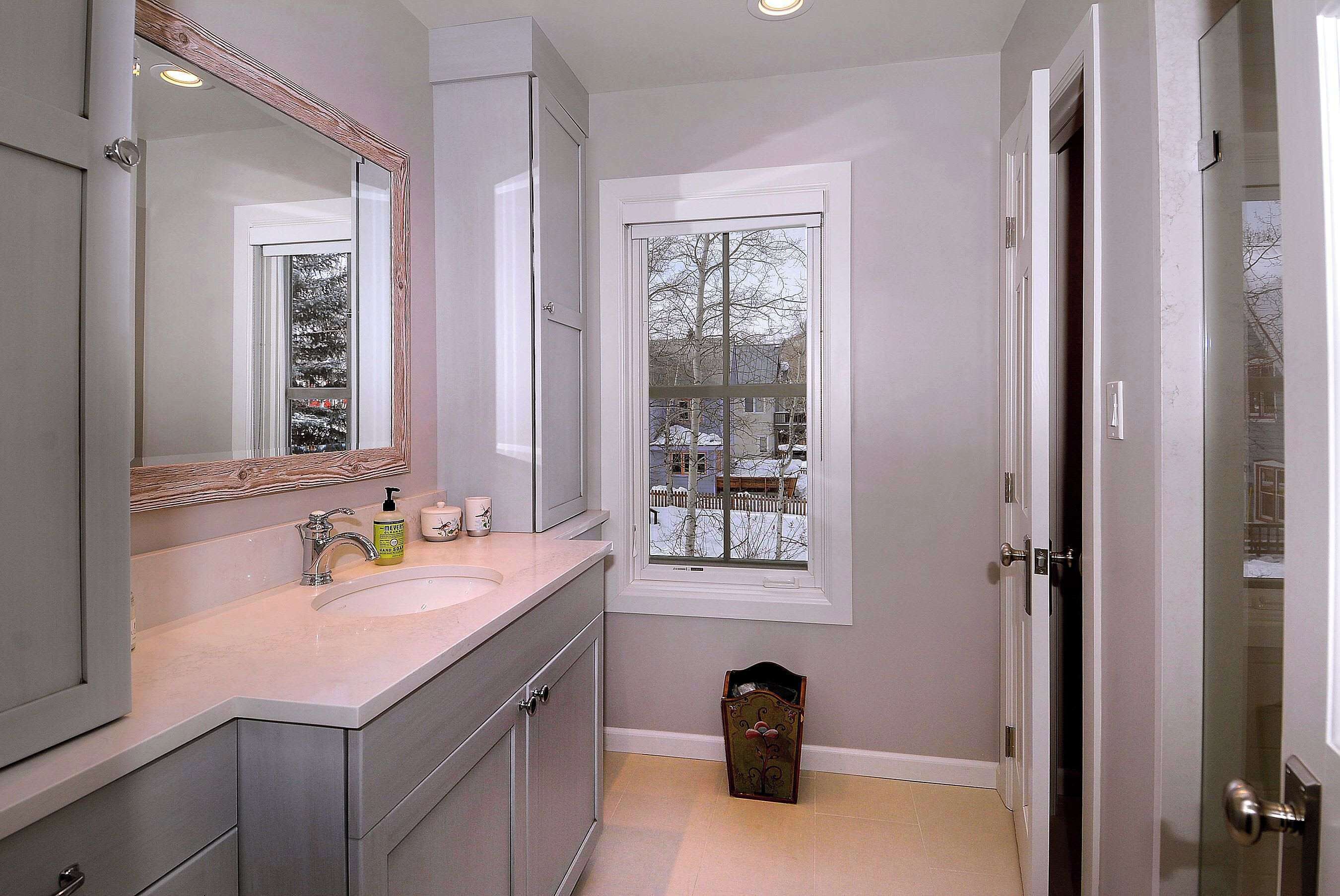 A bathroom with a large mirror, a sink, and a window.