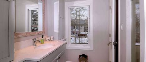 A bathroom with a large mirror, a sink, and a window.