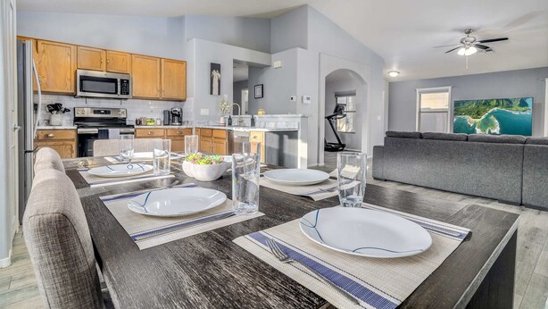 A modern kitchen with wooden cabinets, a microwave, and a dining area with a dark wooden table set for four. - Pool! Workout Room, Treadmill, Grill, Pet Friendly! (Peoria)