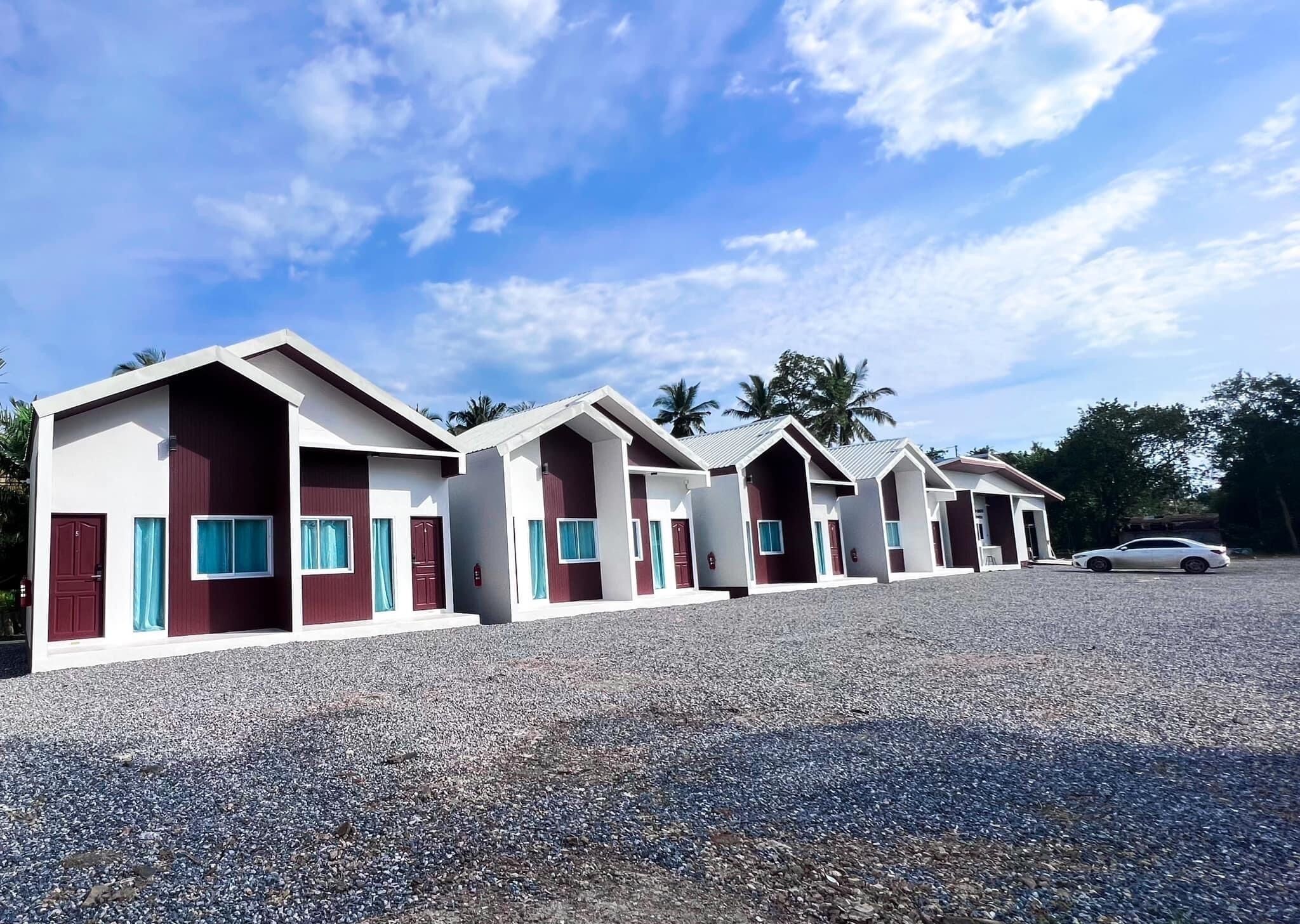 A row of single-story cabins with a gravel driveway, each with a door and windows, and a car parked nearby.