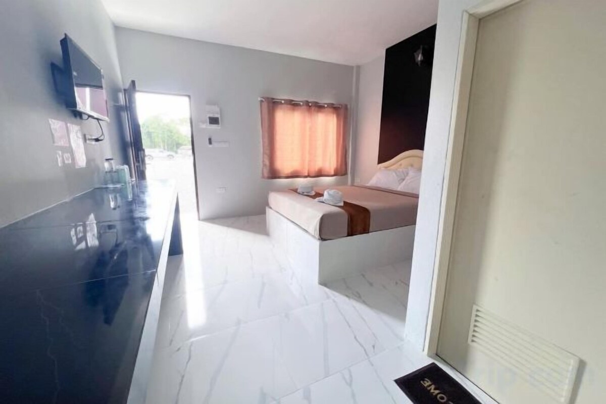 A hotel room with a bed, a small seating area, a TV, and a door with a sign.