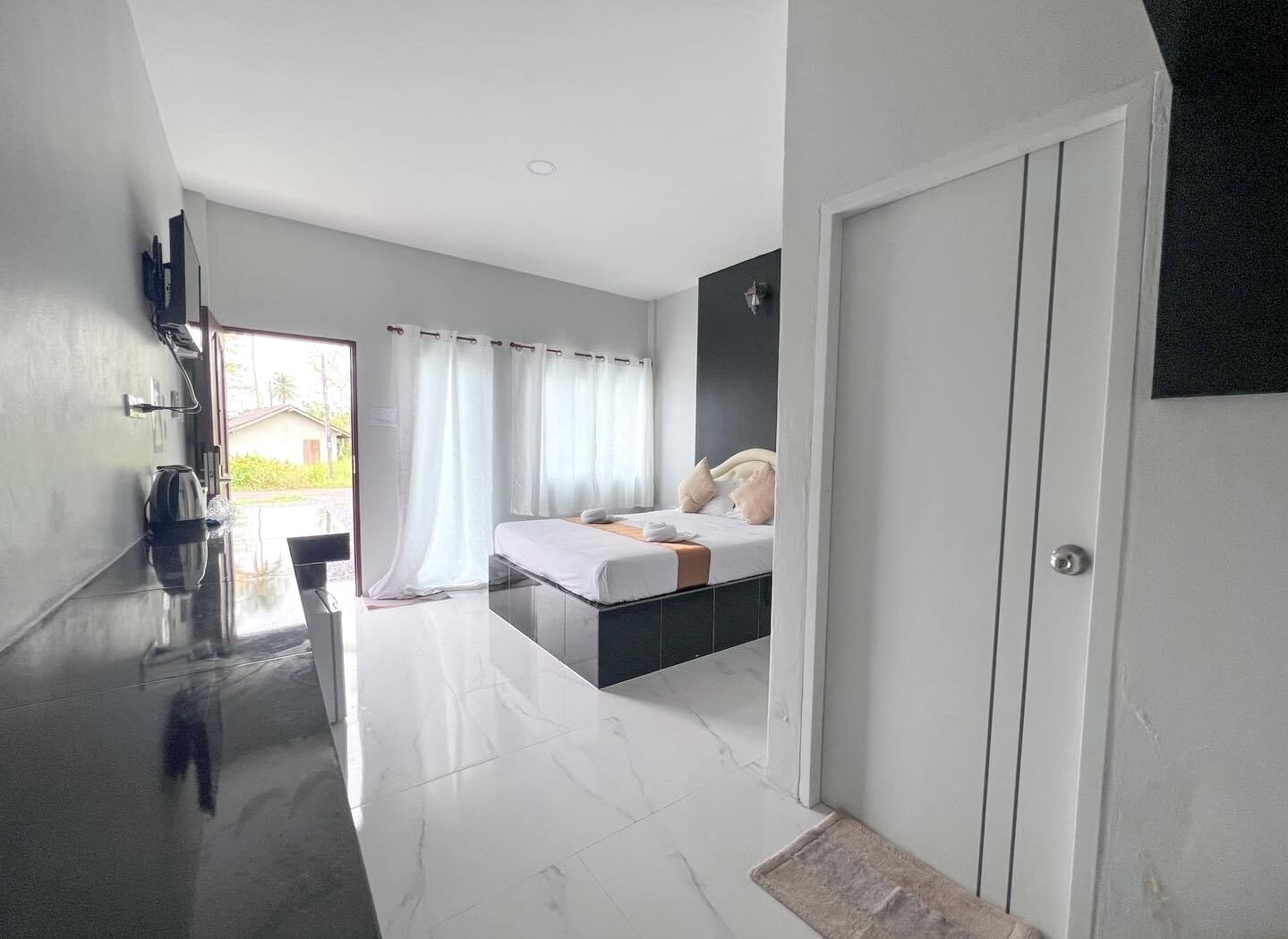 A modern hotel room with a bed, a TV, a kettle, and a view of the outdoors.