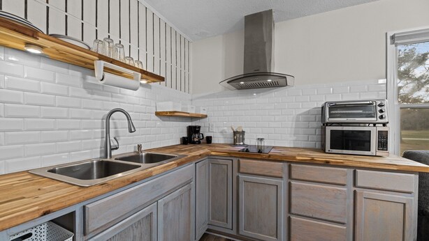 A kitchen with white subway tiles, wooden countertops, a stainless steel sink, a built-in oven, and a range hood. - Renovated Rustic Charm! (New Bern)