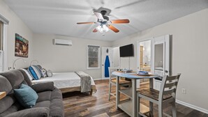 Et lille værelse med seng, sofa, spisebord og ventilator.