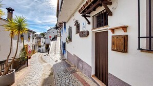 Une ruelle étroite pavée, bordée de bâtiments blancs aux volets et balcons en bois.