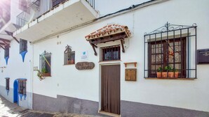 Un bâtiment traditionnel avec un toit en tuiles, une porte en bois et une fenêtre ornée d’une grille en métal.