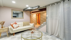A living room with a sofa, a round coffee table, a mirror, and a staircase leading to an upper floor. - Quaint Studio w/ Sauna: 5 Mi to Space Needle (Seattle)