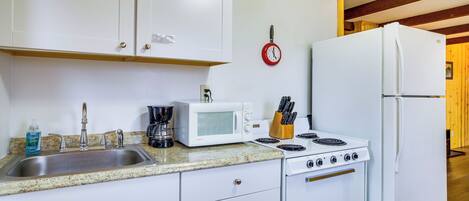 A kitchen with white cabinets, a sink, a microwave, a stove, and a refrigerator.