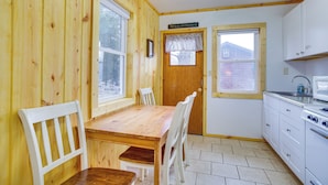 A wooden interior with a dining table and chairs, a kitchen with white cabinets, and a window with a view of a brick building.