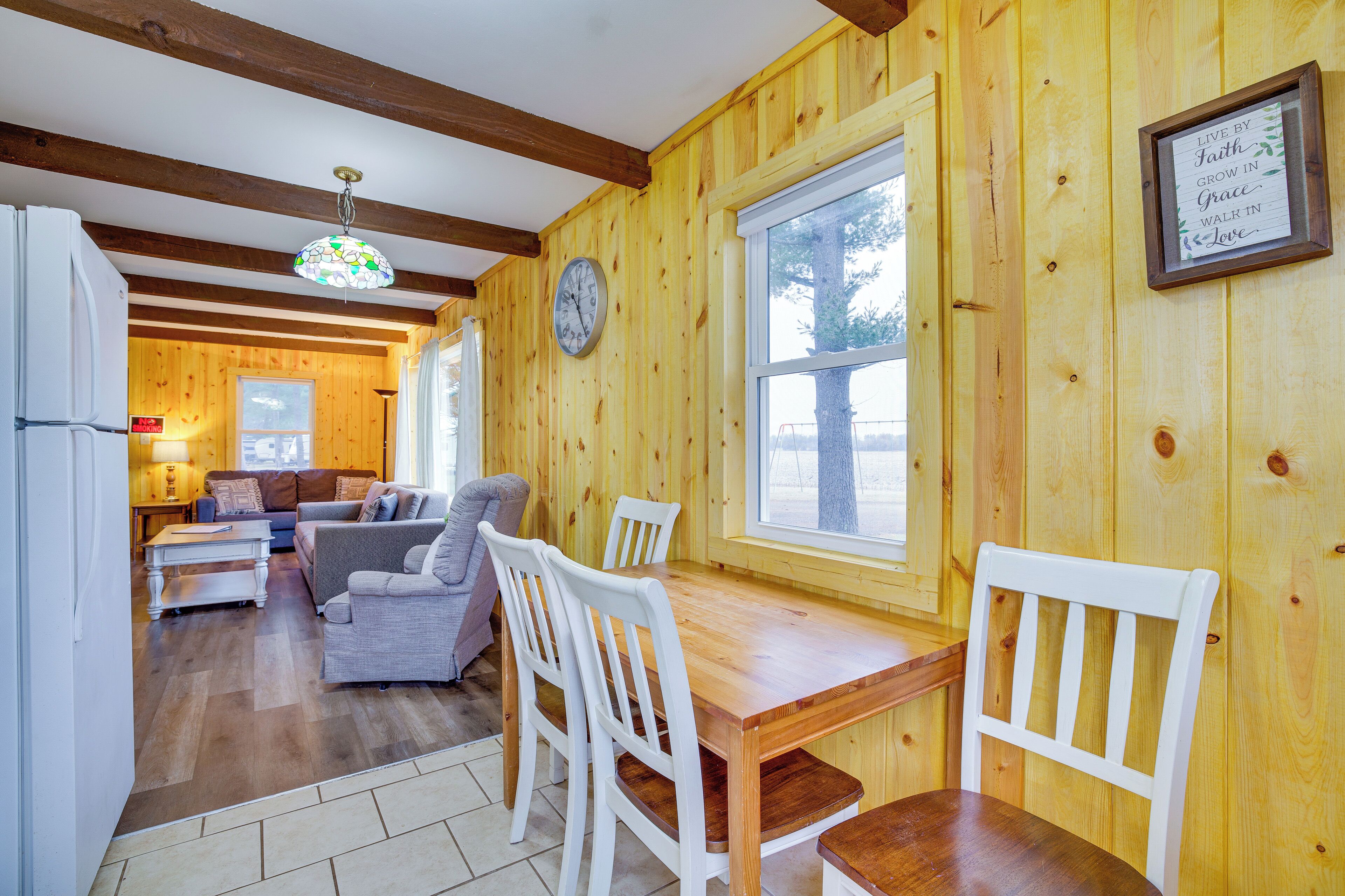 A wooden interior with a dining table, chairs, a sofa, and a clock on the wall.