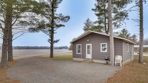 A small cabin with a gravel driveway, surrounded by trees.
