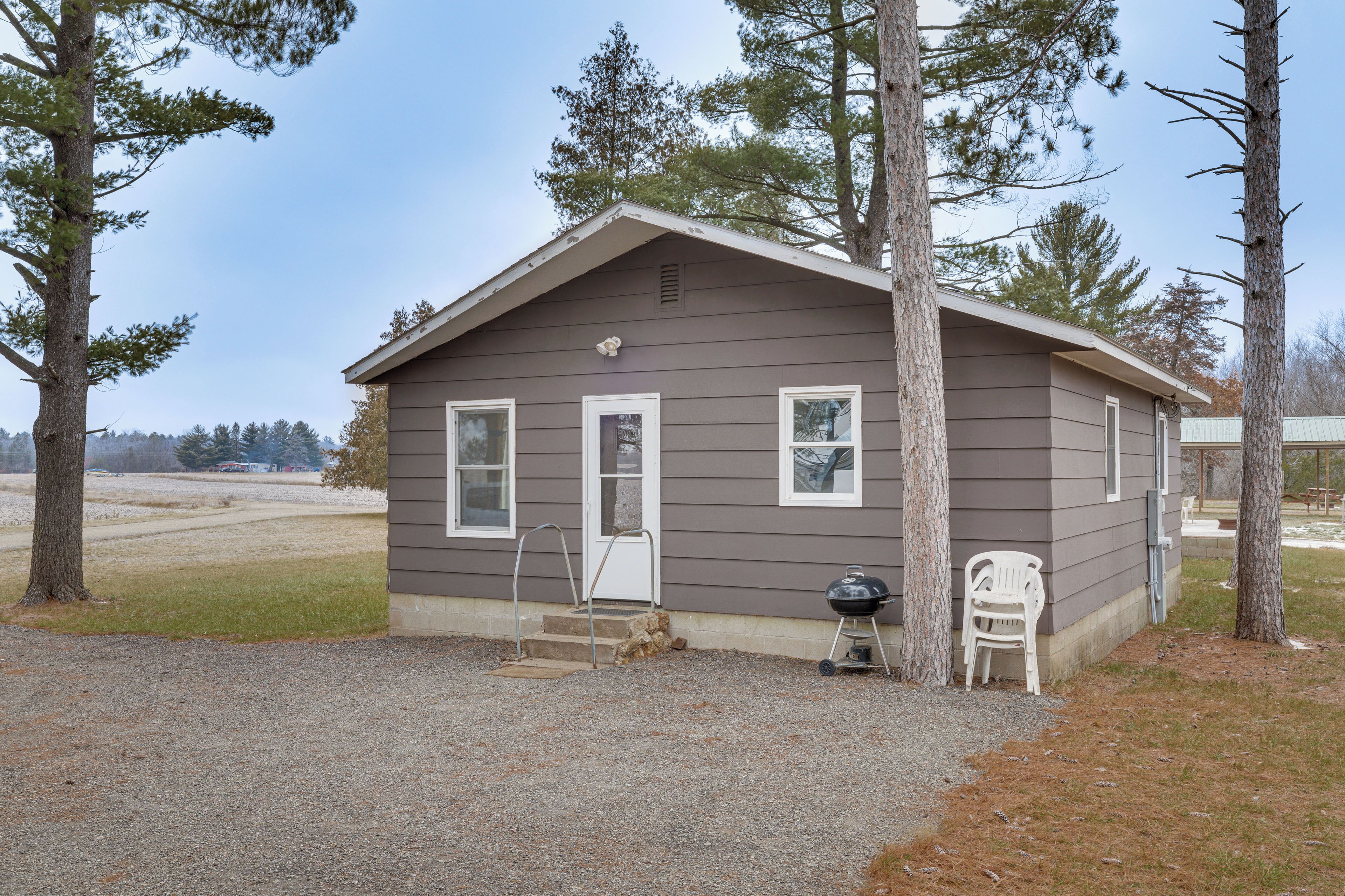 A small, single-story cabin with a front porch, a grill, and a chair.