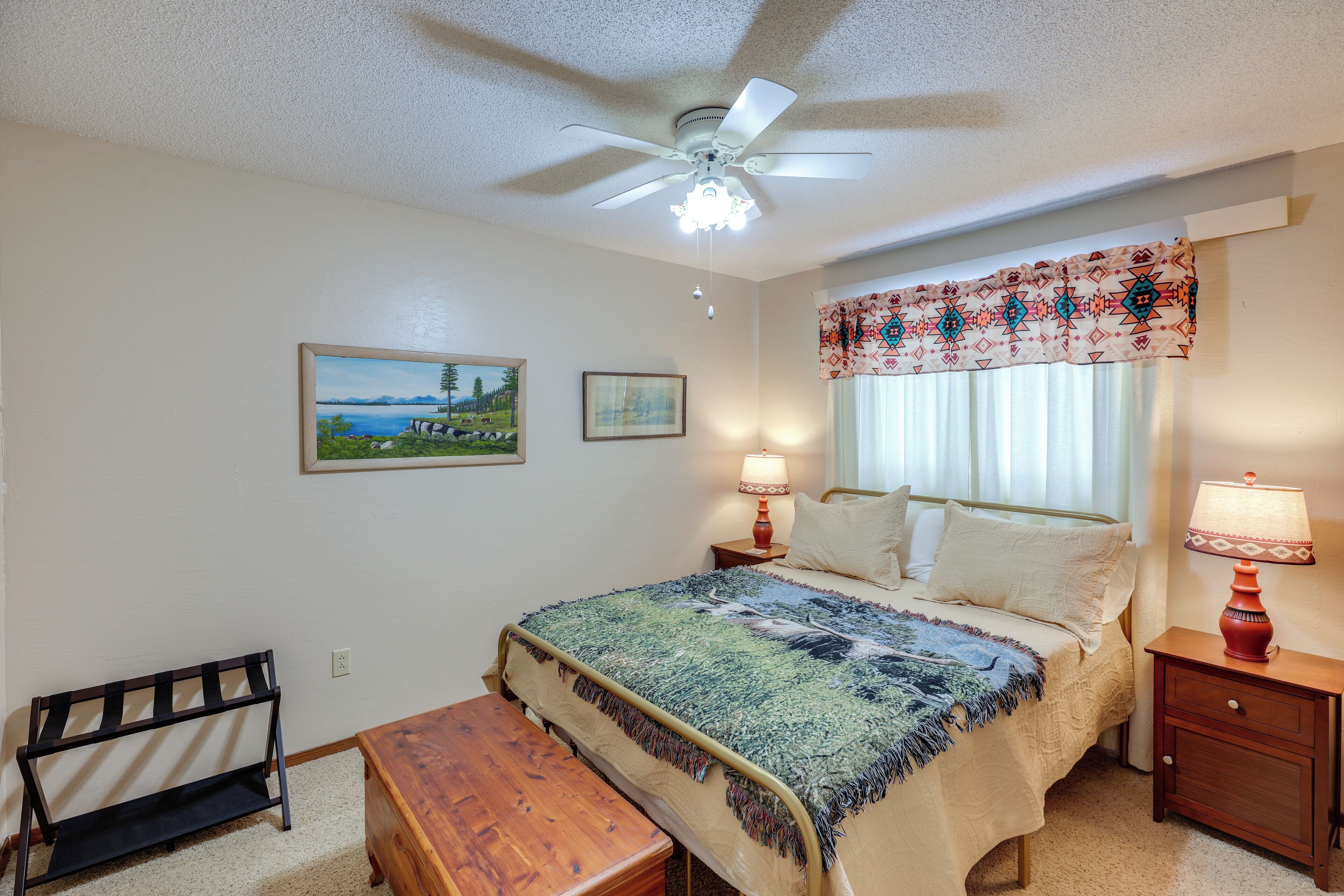 A bedroom with a bed, a bench, a nightstand, a lamp, a ceiling fan, and two framed pictures on the wall.