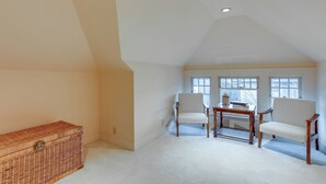 A room with a sloped ceiling, two white chairs, a small wooden table, and a wicker chest of drawers. - Inviting Seattle Apartment: 4 Mi to Ballard Locks (Seattle)