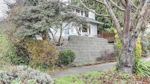 A house with a stone wall, a driveway, and surrounding trees. - Inviting Seattle Apartment: 4 Mi to Ballard Locks (Seattle)